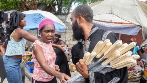 Getty Images A woman reaches across to a stack of machetes being held by a man.