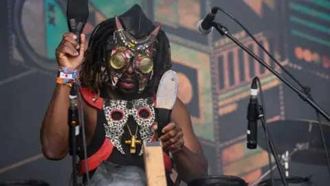 Leon Neal/Getty Images A member of the Democratic Republic of Congo band Fulu Miziki wearing a mask prepares the stage for his bands performance