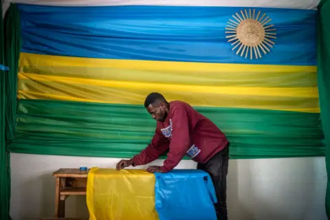 LUIS TATO/AFP a man decorates this polling station in Kigali with green, yellow and blue.