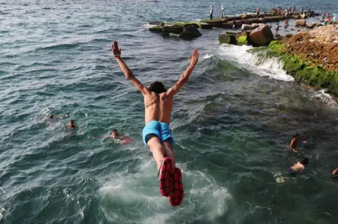 HAZEM GOUDA/AFP Boys swim at the sea, on of them is diving in.