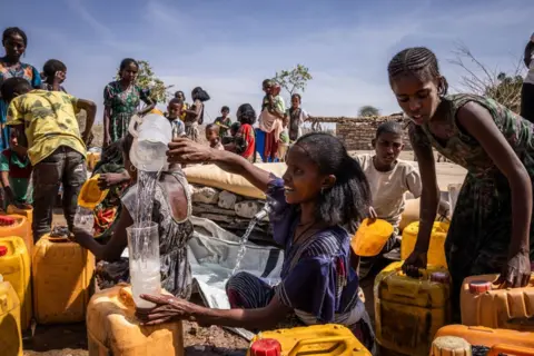 Ed Ram/Getty A woman pours water in to a plastic bottle and fill larger yellow cans with water