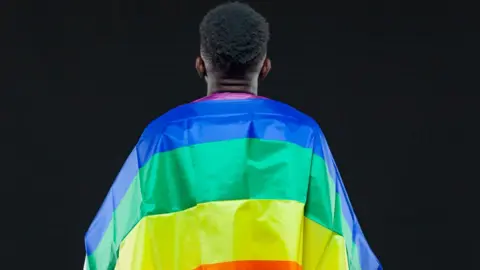 Getty Images A man wrapped in a rainbow flag against a black background