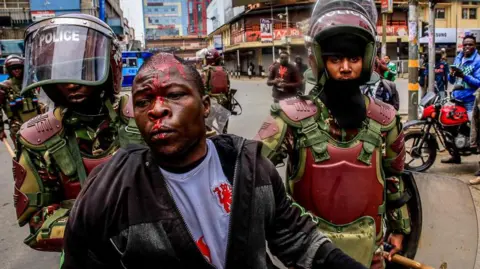 Getty Images Riot police help a protester from being beaten by business operators during a demonstration over police killings of people protesting against Kenya's proposed finance bill 2024/2025 in Nairobi. (