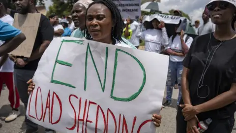 Getty Images People, holding banners, stage a protest against energy crisis after electricity outages for long periods of time in Johannesburg, South Africa on February 02, 2023