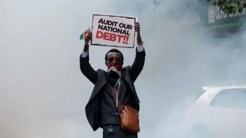 AFP A protester holds a placard as a cloud of teargas surrounds him during an anti-government protests in Nairobi on July 16, 2024