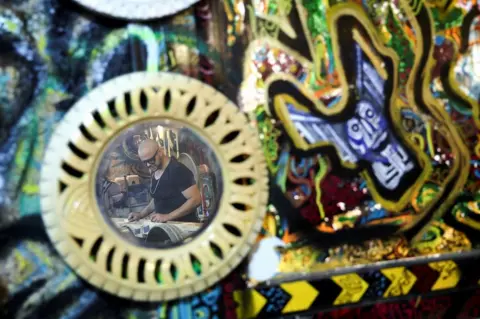 AMR ABDALLAH DALSH / REUTERS A man is reflected in a mirror made of recycled car tyres. 