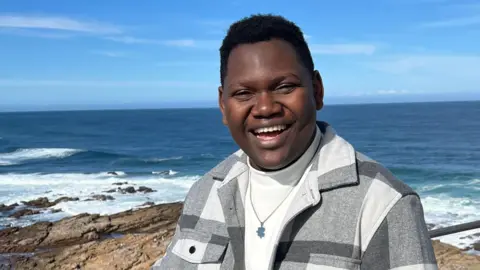 Carina Cristovao Rodwin Malinga with a beautiful blue ocean and sky behind him