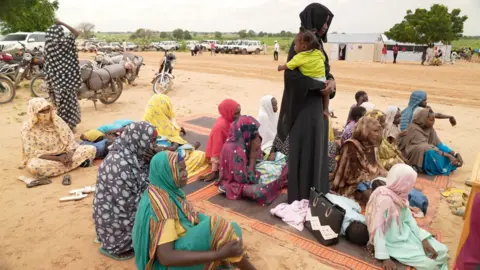 Kevin McGregor / BBC Women sitting on mats on the ground at a camp in Adré 