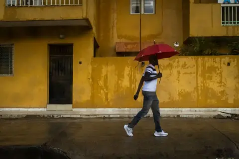 JOHN WESSELS / AFP A man with an umbrella walks down a street during Senegal's rainy season.