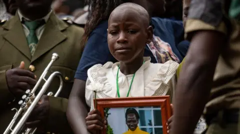 Badru Katumba/AFP An image of Rebecca Cheptegei's youngest daughter crying at her funeral while she holds a picture of her mother in Bukwo district in Uganda - Saturday 14 September 2024.