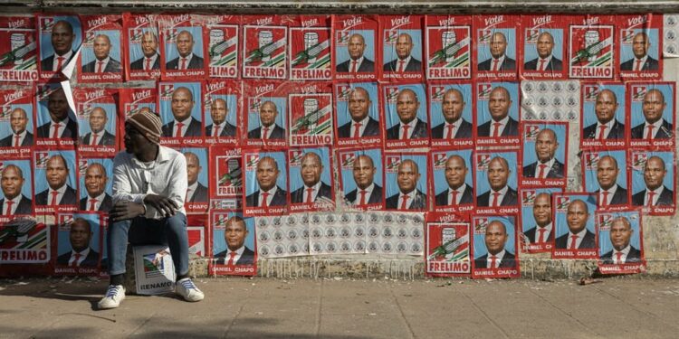 A man sits next to a wall covered with Mozambique Liberation Front (FRELIMO) electoral posters during the first day of the 2024 presidential campaign ahead of the 9 October 2024 national election in Maputo. (Alfredo Zuniga/ AFP)