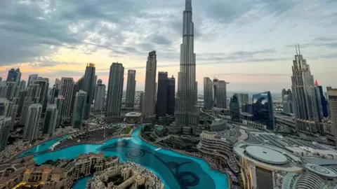 Reuters A view of the Dubai skyline backing onto a brightening sky featuring several skyscrapers and a man-made canal full of glistening blue water