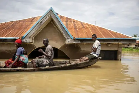 OLYMPIA DE MAISMONT/AFP Residents sit in a pirogue as they move between submerged houses in the flooded area of Adankolo in Lokoja, Kogi state, Nigeria.