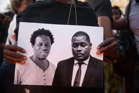 ALFREDO ZUNIGA/AFP An image is held of Paulo Guambe (L) and advisor and lawyer Elvino Dias (R) both working with Mozambique's leading opposition candidate for the 'Obtimist party for the development of Mozambique' (PODEMOS), is held during a vigil the day after they were shot dead in Maputo October 19, 2024. The lawyer Elvino Dias for Mozambique's leading opposition candidate Venancio Mondlane, who ran for president in October 9 elections, was gunned down in Maputo on October 19. Dias, was killed along with Paulo Guambe after gunmen shot up their car while it was immobile on a road in the centre of the capital, witnesses said. Mozambique is awaiting official nationwide results from the elections. They are due to be published on October 24.