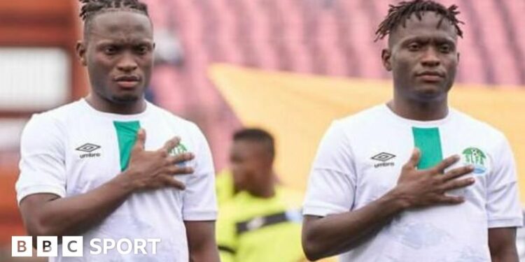 Identical twins Alhassan and Alusine Koroma, wearing white Sierra Leone shirts, both stand with their right hand over their heart during the national anthem