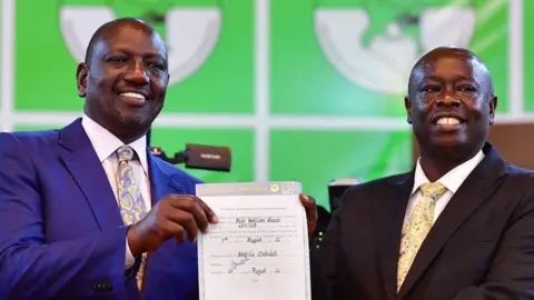 AFP Both wearing suits, William Ruto stands with Rigathi Gachagua holding a certificate of election between them in an archive picture from 2022.