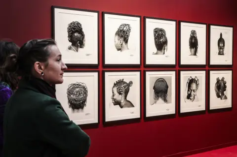 Teresa Suarez / EPA People walk past 10 framed photographs of different braided hairstyles hung on a wall painted maroon during the Paris Photo fair at the Grand Palais in Paris, France -  Wednesday 6 November 2024