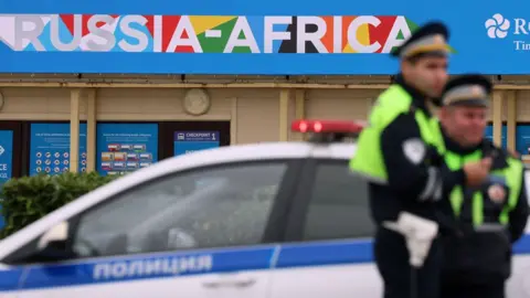 AFP Two traffic police officers near a police car stand guard on a roadside with branding for the Russia-Africa summit seen behind them in Sochi, Russia - 8 November 2024