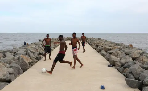 SIPHIWE SIBEKO / REUTERS Teenagers play soccer on a concrete beach pathway in Maputo.