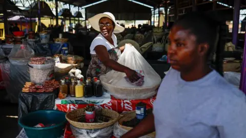 AFP A woman at a market stall with a wide-brimmed hat on cleans a clear plastic bag protecting a basket of sugar. 