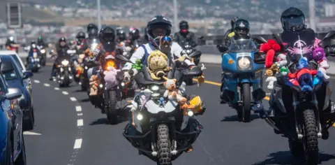 Brenton Geach /  Getty Images People drive motorbikes in a convoy. Plush toys are fastened on to the bikes.