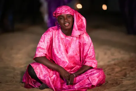 Cem Ozdel / Getty Images A woman sits cross-legged on the ground and sings.