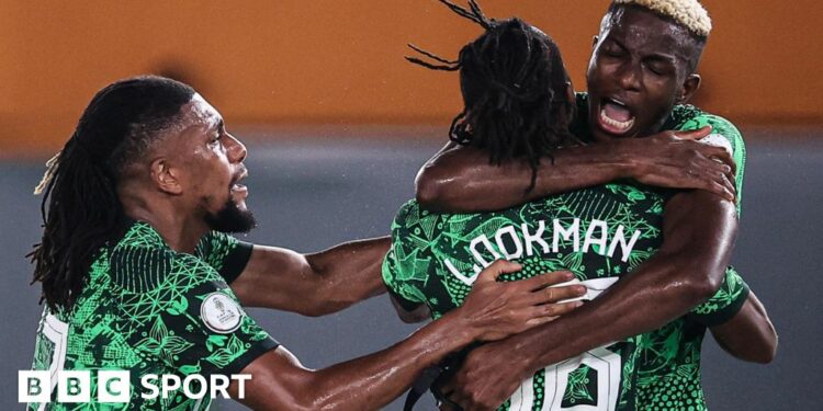 Nigeria players celebrate a goal, with Victor Osimhen giving Ademola Lookman, who is facing away from camera, a hug as Alex Iwobi joins the embrace from the left of the shot