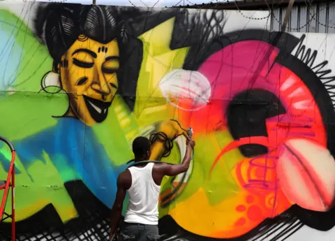 LEGNAN KOULA / EPA A man spray-paints a mural in bright colours on a large concrete wall in Abidjan.
