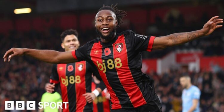 Antoine Semenyo, wearing a red and black striped Bournemouth strip, stretches his arms out wide and smiles while celebrating a goal against Manchester City