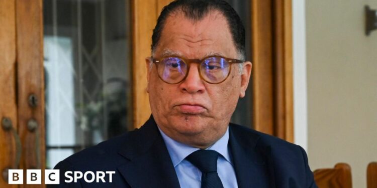 Danny Jordaan, pictured wearing glasses and a dark blue suit with a light blue shirt and dark blue tie