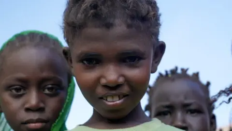 Joyce Liu / BBC Three children in Sudan stare directly at the camera