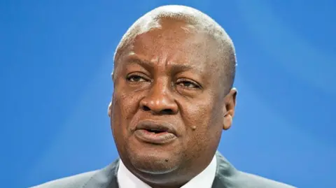 Getty Images Ghanaian President John Dramani Mahama speaks at a press conference, with a blue backgroud behind him