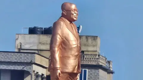 Citi Newsroom The statue of Nana Akufo-Addo, which is bronze in colour. He is in profile, depicted wearing a suit, his glasses and is smiling. It is outside Effia-Nkwanta Regional Hospital in Sekondi, Ghana - November 2024