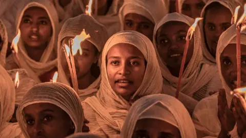 AFP Orthodox Christian women wearing white head scarves and holding candles  at prayers ahead of Christmas celebrations at the Bole Medhanialem Church in Addis Ababa - 6 January 2024