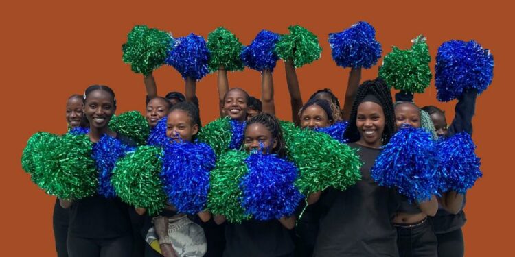 A group of female cheerleaders dressed in black stand and hold up green and blue pom poms