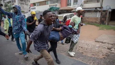 AFP A group of male protesters carry another protester injured by a rubber bullet fired by riot police in Maputo