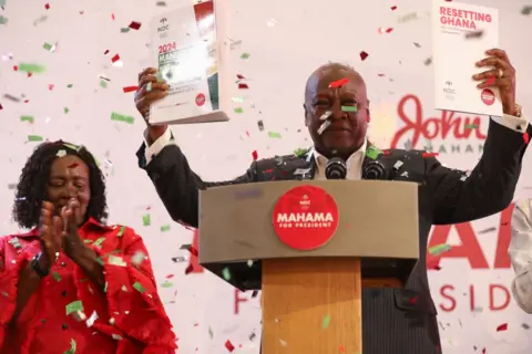 AFP John Mahama (R), holds a copy of the party's manifesto as his running mate Jane Naana Opoku-Agyemang (L),  looks on in Winneba, Ghana, on August 24, 2024