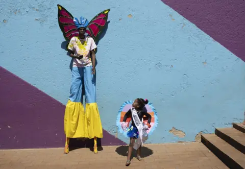 KIM LUDBROOK / EPA Stilt-walker Andile Sohe (32) and Miss Preteen Orange Farm, Thando Mbatha (7) pose for the camera.