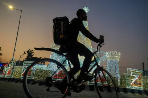 MARVELLOUS DUROWAIYE / REUTERS A cyclist passes illuminated Christmas lights.