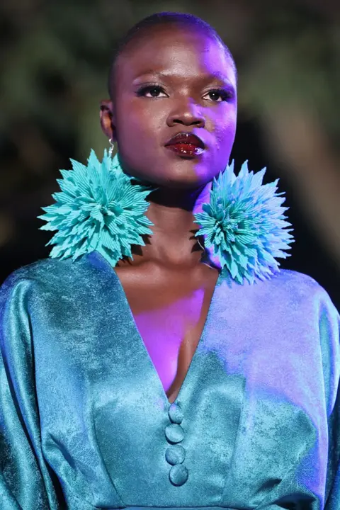 Cem Ozdel / Getty Images A woman wears a large turquoise pair of pom-pom earrings and a satin dress of a similar shade. Her lipstick is a deep berry colour. In Dakar, Senegal - Saturday 7 December 2024