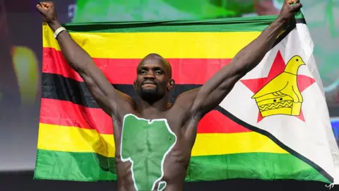 Chris Unger / Getty Images A muscled man with the outline of the African continent daubed on his torso in green holds up the Zimbabwe national flag above his head in Las Vegas, the US - Friday 6 December 2024