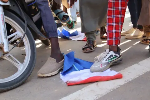 Denis Sassou Gueipeur / AFP People stamp on a French national flag. Only their legs and feet are visible. On a street in N'Djamen, Chad - Friday 6 December 2024