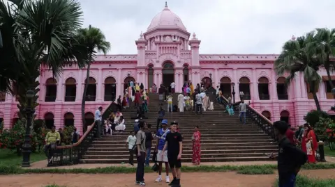 Kids of the Colony Zak Hajjaj, Abu Finiin, Kayum Miah standing outside the steps of the pink palace (Ahsan Manzil) in Dhaka, Bangladesh surrounded by people