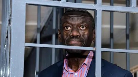 Reuters Kizza Besigye looks through a metal grille at the Uganda Military General Court Martial that sits in Makindye suburb of Kampala, Uganda November 20, 2024