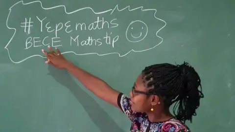 Angela Tabiri Dr Angela Tabiri look towards and pointing at a blackboard with some maths tips written in chalk during a FemAfricMaths YouTube lesson for junior high school students