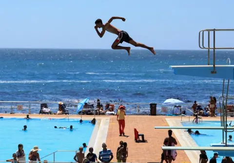 ESA ALEXANDER / REUTERS A person dives from a springboard during a hot summer day at Sea Point swimming pool in Cape Town, South Africa, January 10, 2025. 