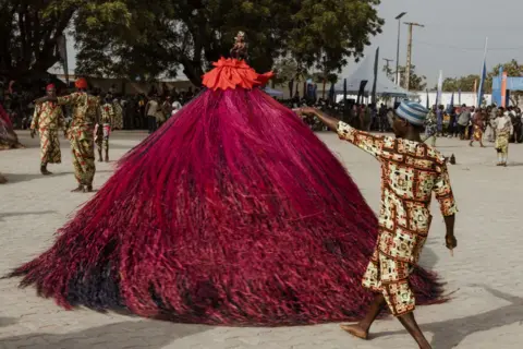 MARCO LONGARI / AFP A person dances in circles wearing a huge swirling costume of long purple tassels,