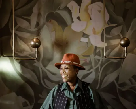 MARCO LONGARI / AFP A women dressed in a trilby, shirt and chef's waistcoat smiles infront of luxurious wallpaper and lighting.