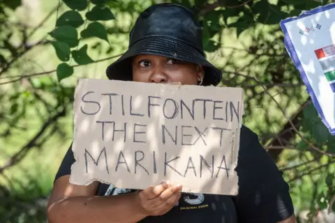 LEON SADIKI / GETTY IMAGES A woman pickets the mine in Stilfontein with a sign that reads: '