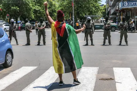 ESTEVAO CHAVISSO / EPA A woman draped in the Mozambique flag squares up to a line of armed policemen and shouts slogans near the Independence Square during the inauguration of Mozambique's fifth president, Daniel Chapo, in Maputo.